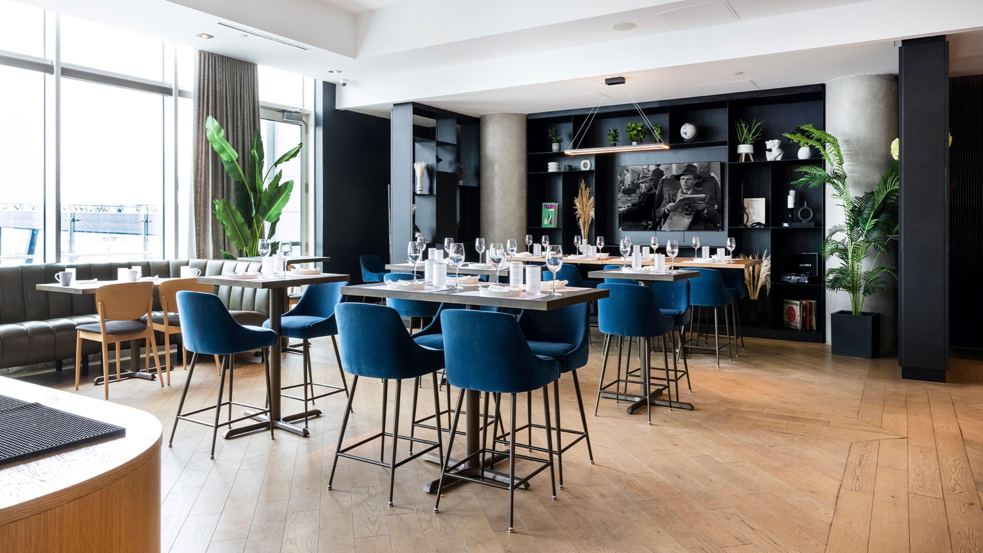 A modern restaurant with high tables, blue chairs, and a black interior.