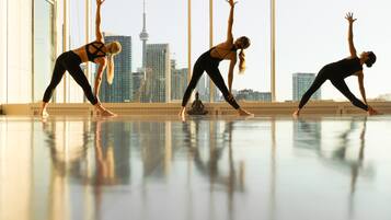Three individuals performing yoga in a spacious room with large windows offering a cityscape view.