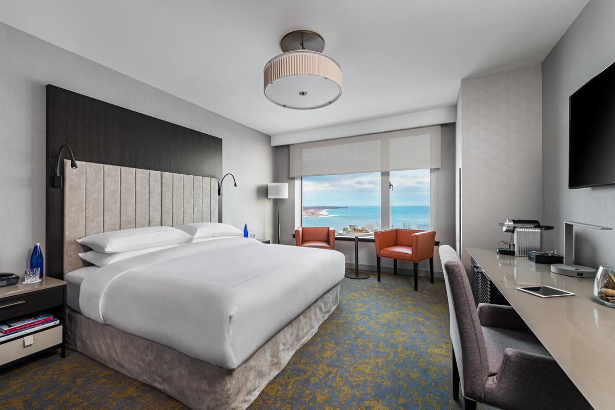 A hotel room with a bed, a desk with a chair, a TV, and a view of the ocean.