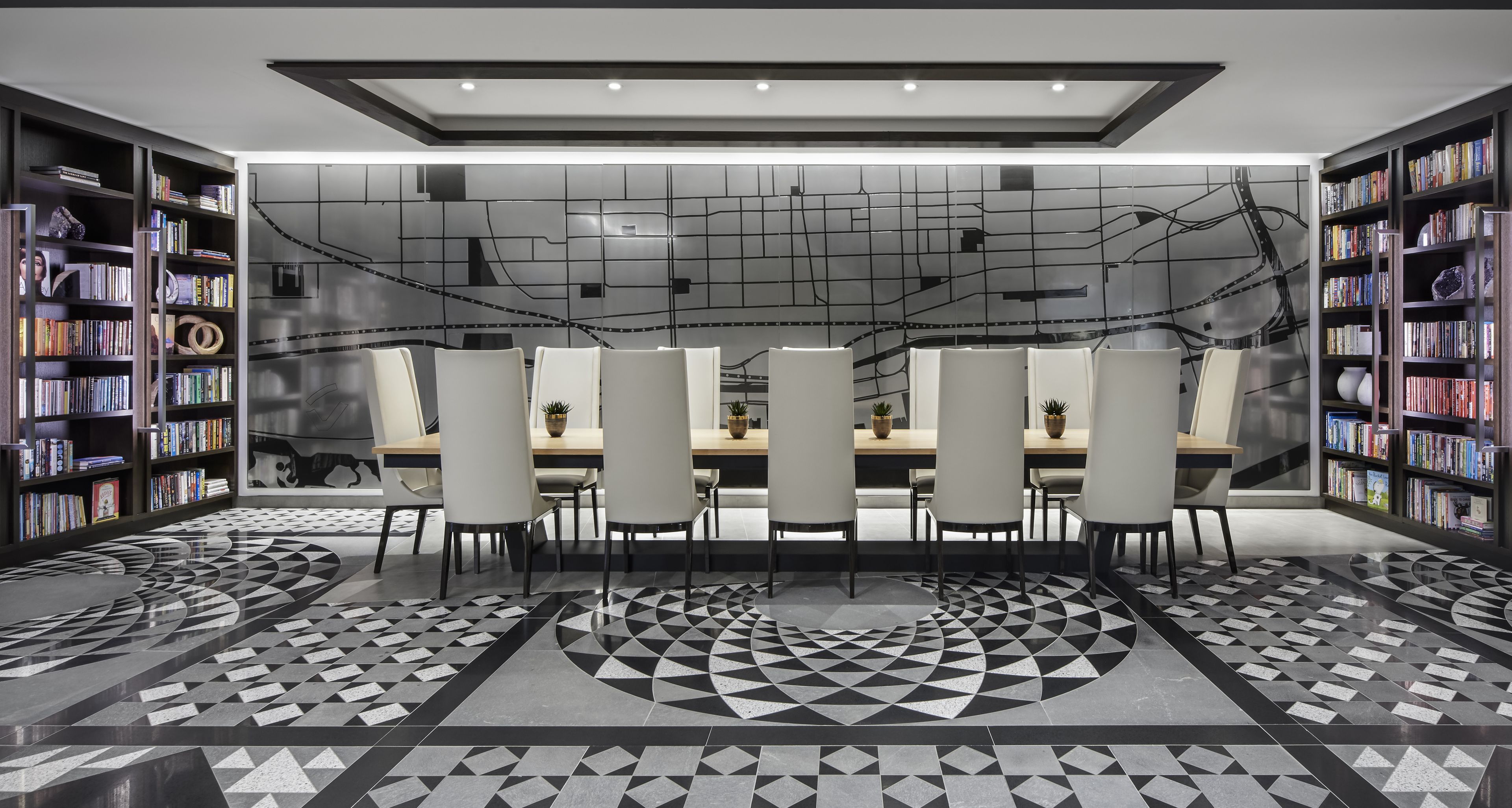 Une bibliothèque moderne dotée d’un sol à motifs géométriques, d’une table centrale entourée de chaises et d’étagères disposées de part et d’autre.