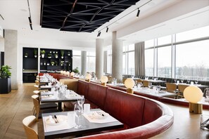 A modern restaurant with long tables, red leather booths, and a large window view. - Hotel X Toronto, a Destination by Hyatt Hotel (Toronto)