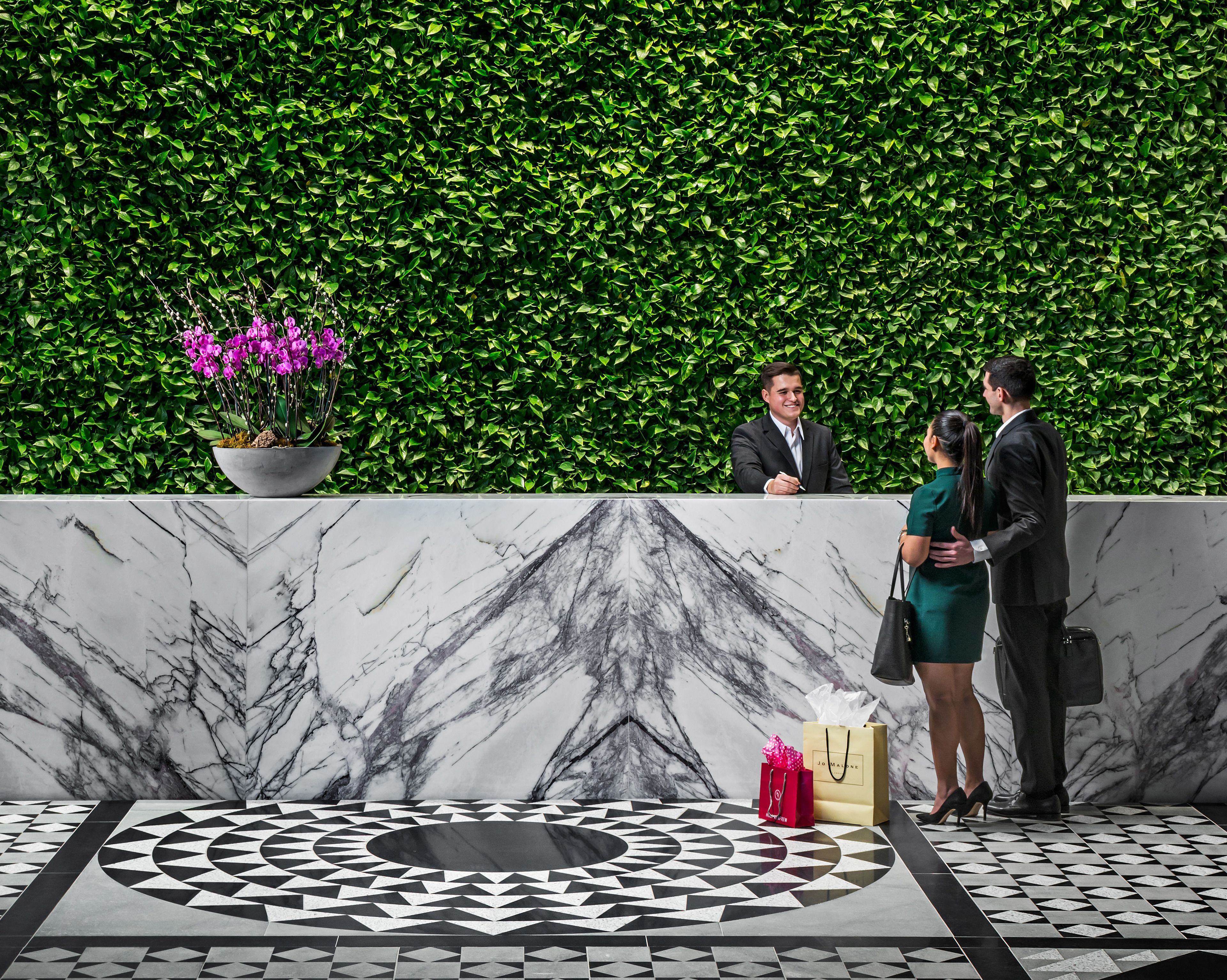 Een receptiezone met een marmeren vloer, een haag als wand en een potplant met paarse bloemen.