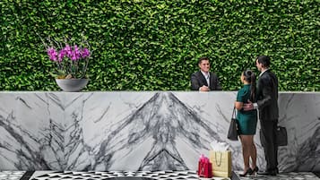 Een receptiezone met een marmeren vloer, een haag als wand en een potplant met paarse bloemen.