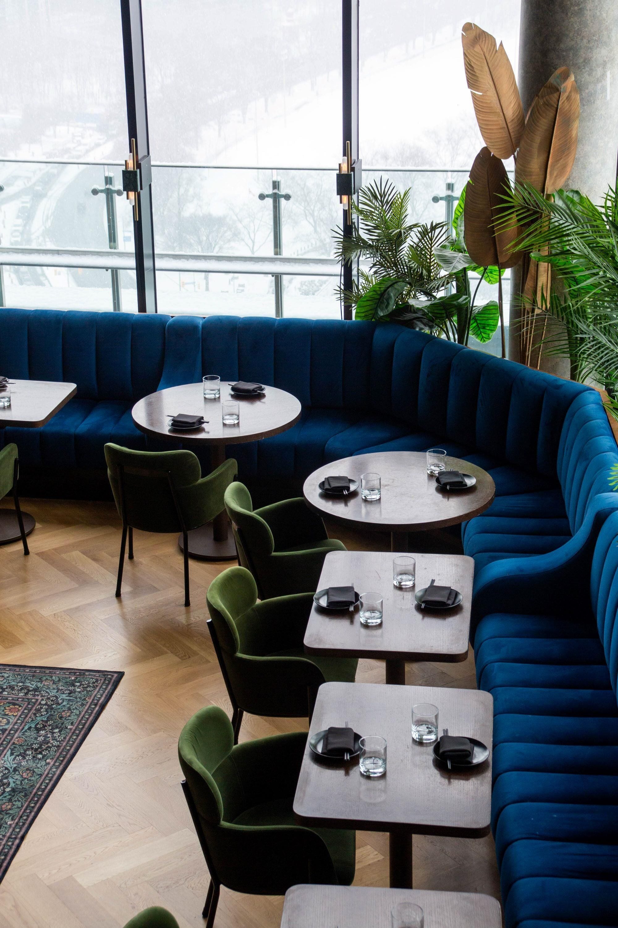 A modern interior with a blue upholstered seating area, round tables, and green chairs.