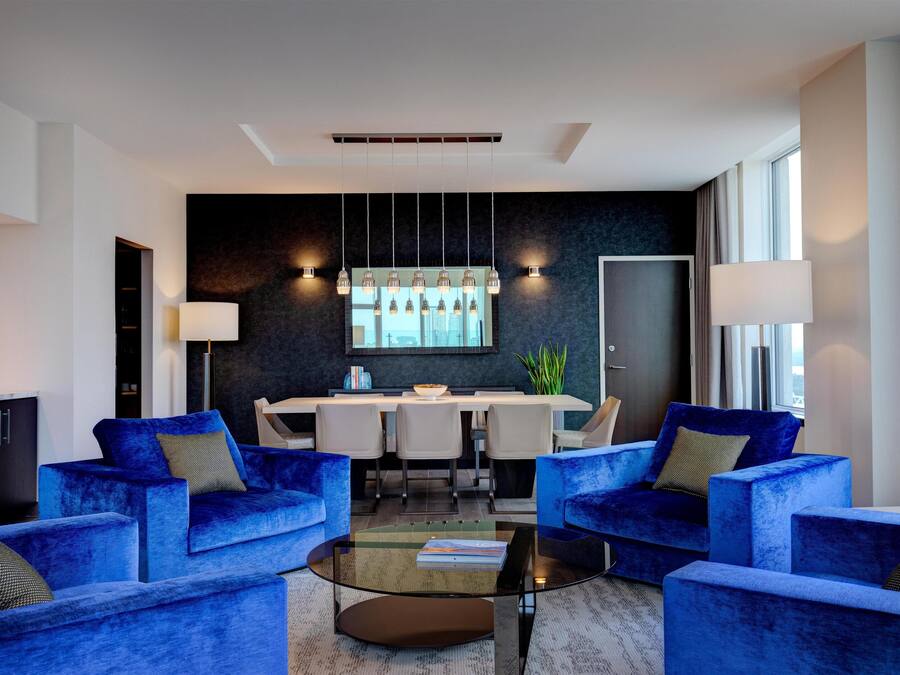 A modern living room with blue sofas, a glass coffee table, and a dining area with a white table and chairs.