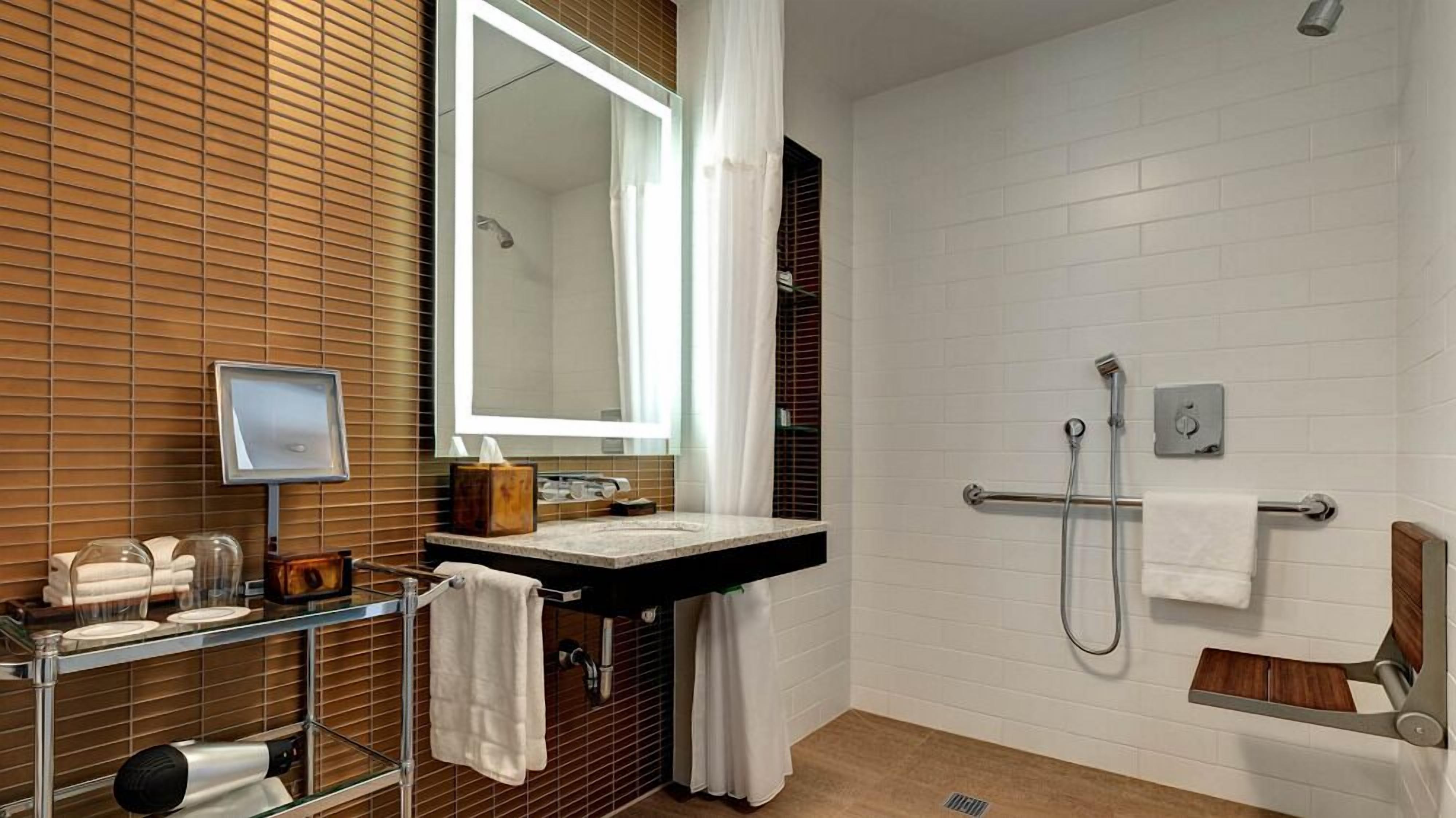 A modern bathroom with a wooden vanity, a large mirror, a shower with a handheld showerhead, and a towel rack.