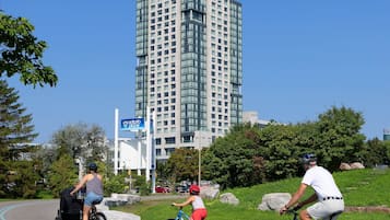 A modern high-rise building with a glass facade, surrounded by greenery and a clear blue sky.