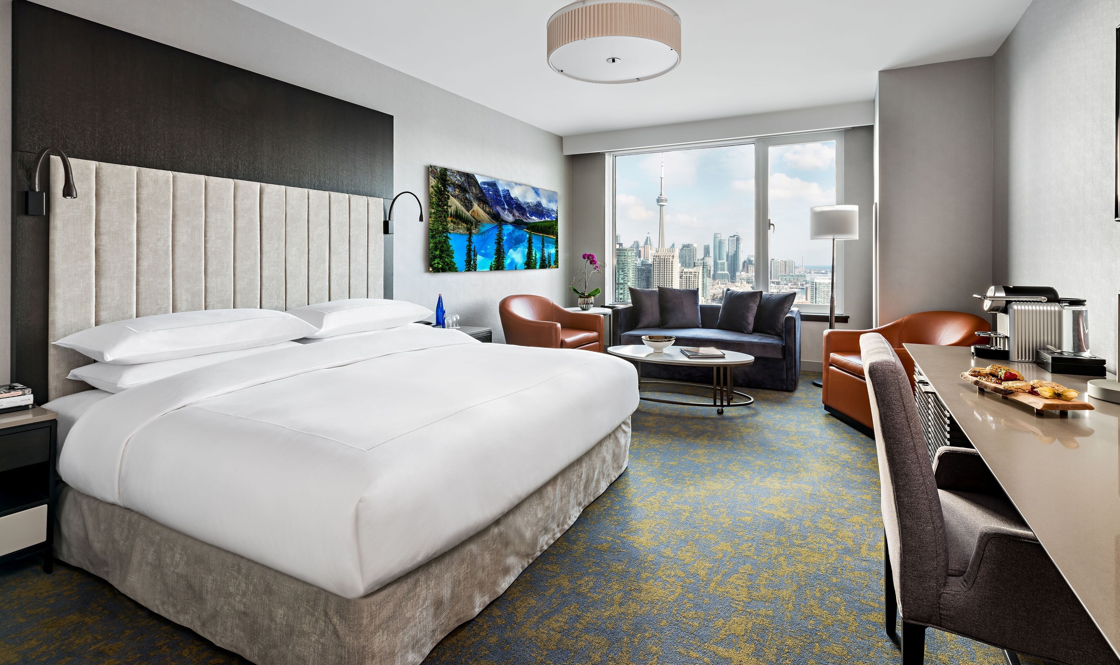 Una habitación de hotel moderna con una cama grande, un sofá, una mesa de comedor y vistas a la ciudad.