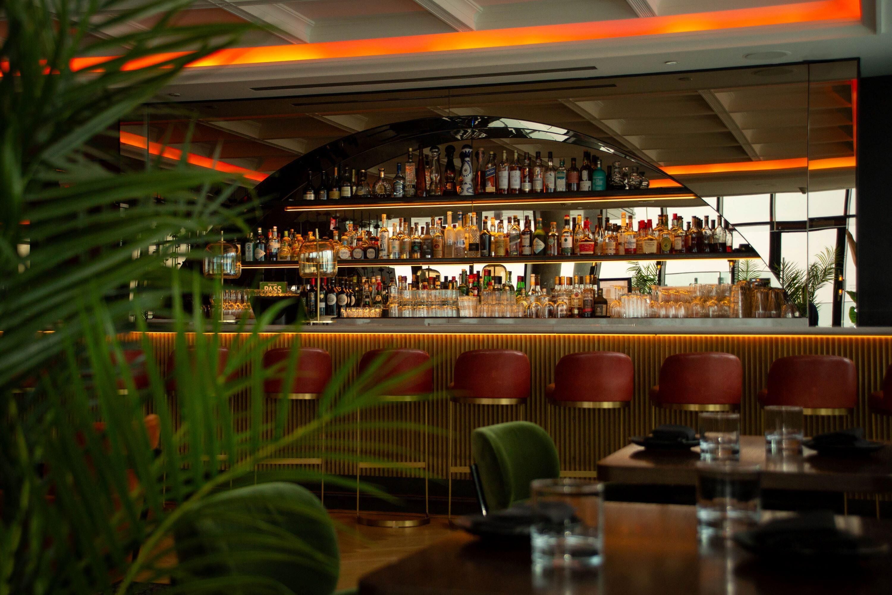 A bar area with shelves of bottles, a counter, and red bar stools.