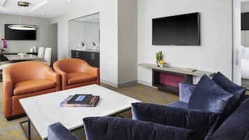 Een moderne woonkamer met een bank, fauteuils, een salontafel en een flatscreen televisie aan de muur.