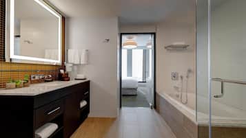 Een moderne badkamer met een grote spiegel, een douchecabine van glas en een zichtbare slaapkamer door een geopende deur.