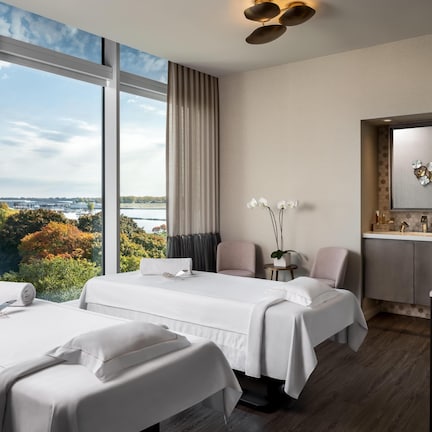 A hotel room with two beds, a large window with a view, a vanity with a mirror, and a small desk.