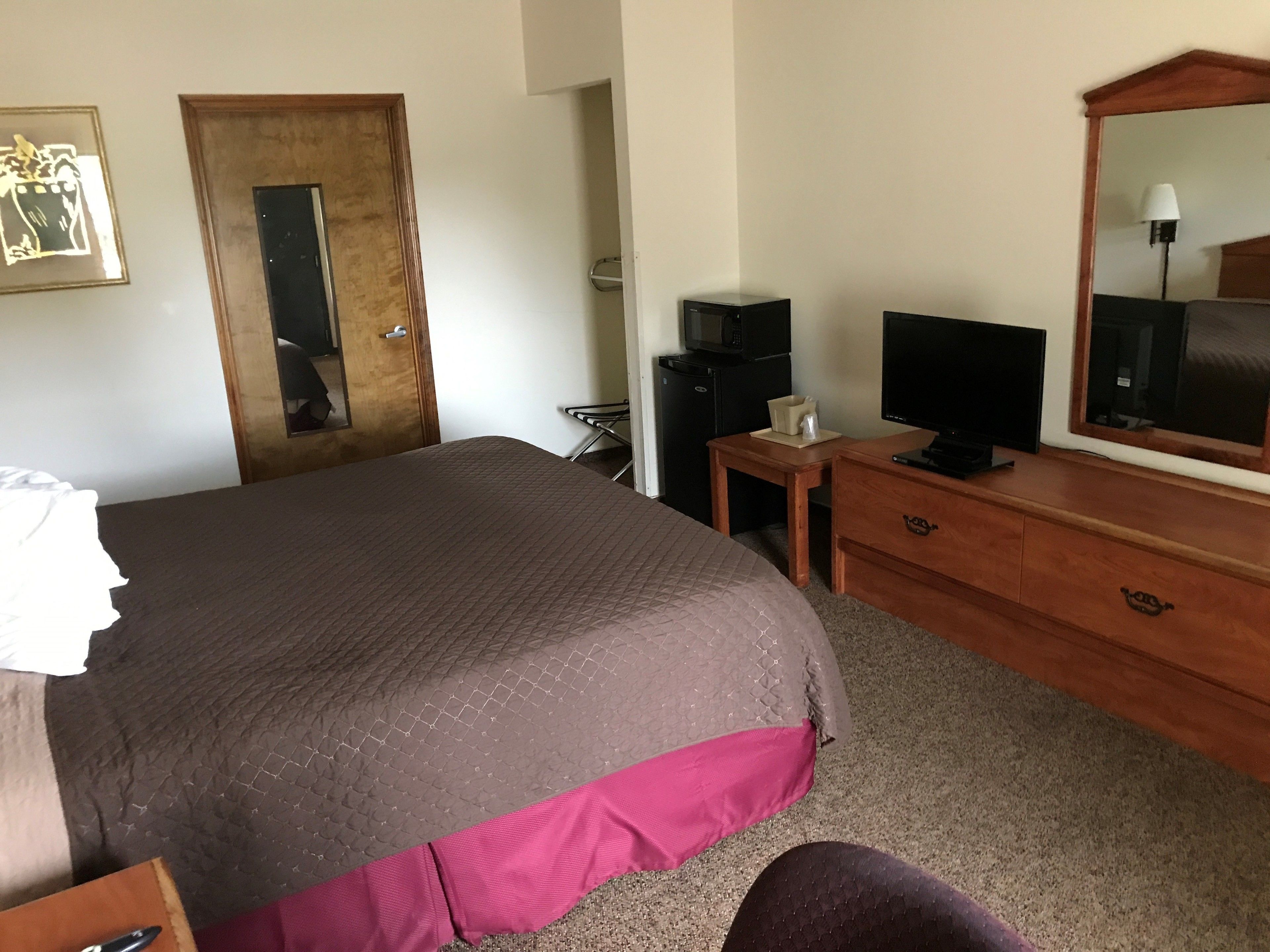A bedroom with a bed, a wooden dresser, a television, and a microwave.