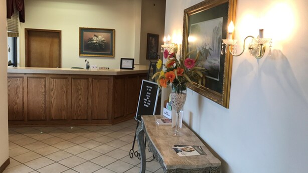 A reception area with a wooden counter, a vase with flowers, a framed picture, and wall sconces.