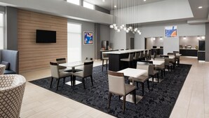 Uma área de refeições moderna em hotel, com pé-direito alto, uma grande mesa de jantar e um bar.