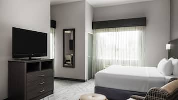 Een moderne hotelkamer met een flatscreen televisie, een groot bed, een bank, een spiegel en een raam met transparante gordijnen.