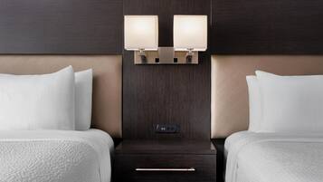A hotel room with two beds, a dark wood headboard, bedside lamps, a control panel, and a drawer.