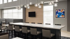 Uma sala de conferências moderna com uma mesa comprida, várias cadeiras, uma TV de tela plana e um grande quadro abstrato na parede.