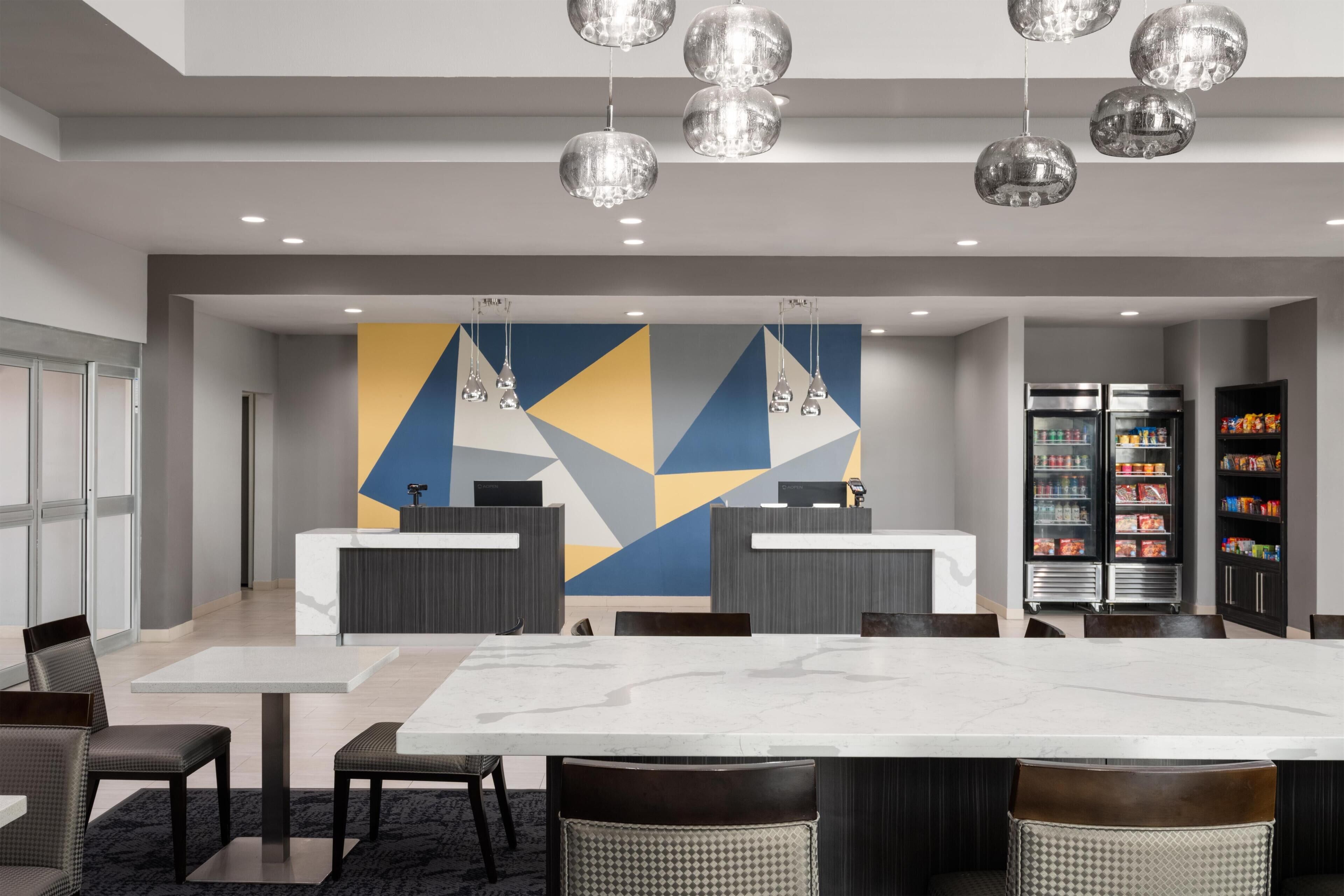 A modern hotel lobby with a reception desk, seating area, and vending machines.