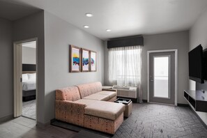A modern hotel room with a sofa, a television, a window with curtains, and artwork on the wall. - Best Western Plus Executive Residency Baytown (Baytown)
