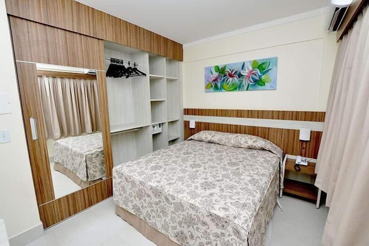 A bedroom with a bed, a wardrobe, a mirror, a painting, and a telephone.
