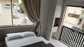 Une chambre à coucher avec un lit, une fenêtre avec des rideaux, un balcon avec une balustrade et une vue sur l’extérieur.