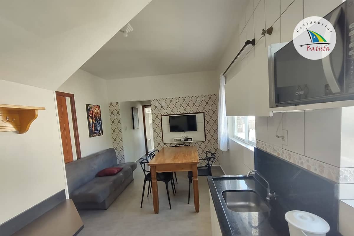 Ett modernt kök med en matplats, en grå soffa, en tv och ett fönster.