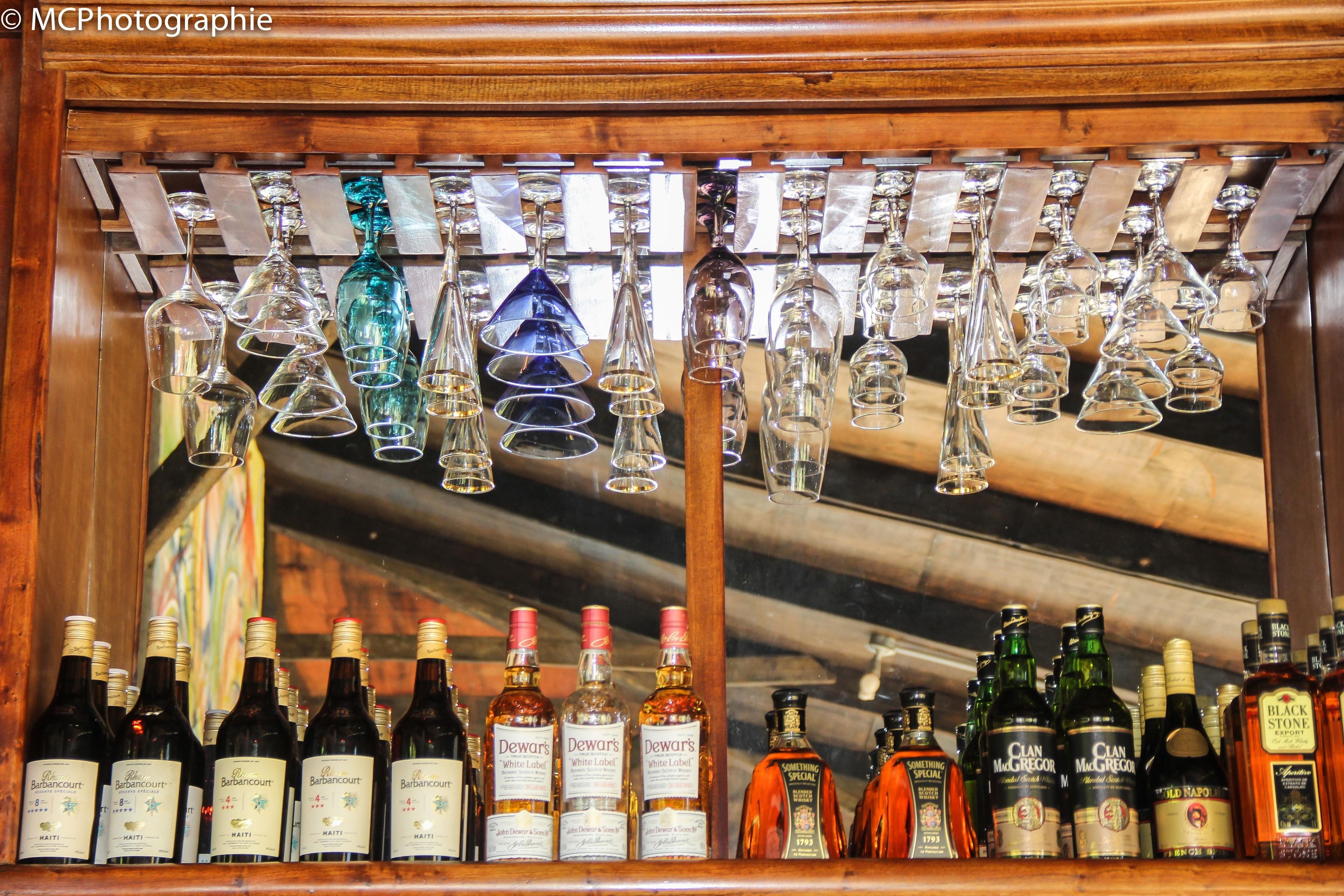 Un bar con varias botellas y vasos en estantes y colgando del techo.
