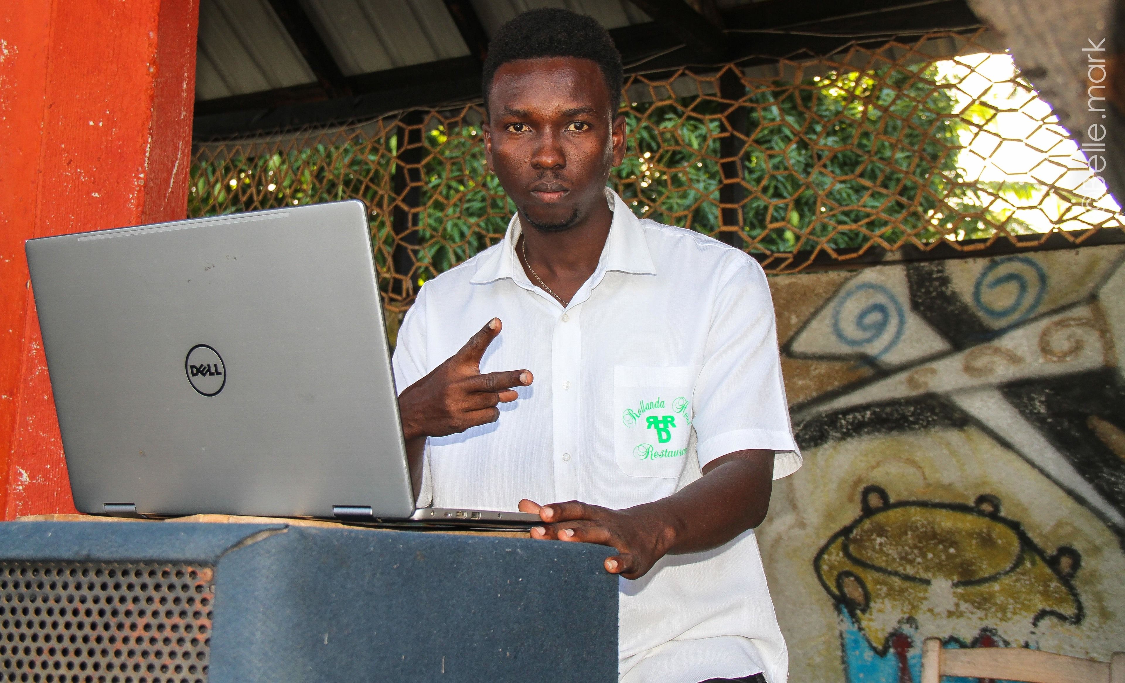 A person standing behind a podium with a laptop, wearing a white shirt with a logo.