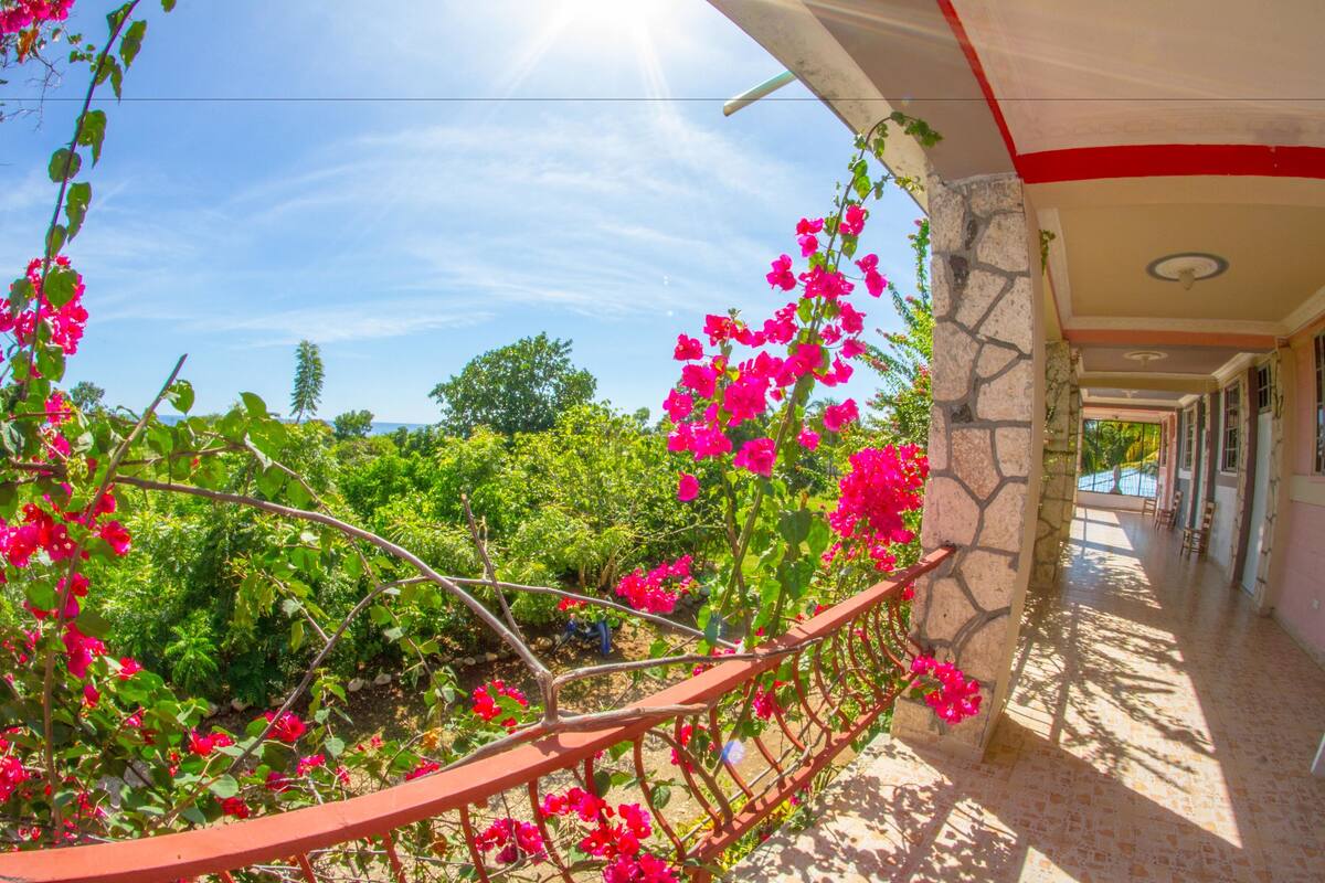 A balcony with a view of a garden, a stone wall, and a tiled floor.