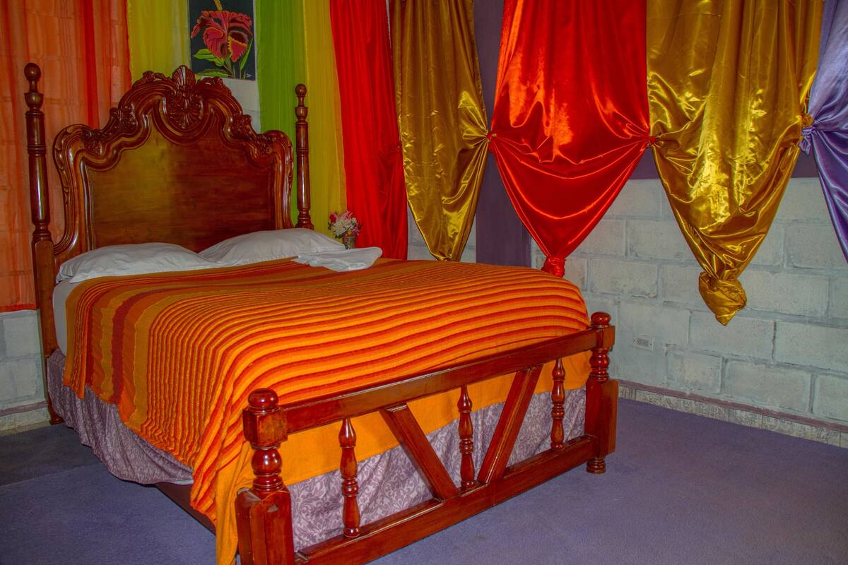 A bed with a wooden headboard, a striped orange bedspread, and red and gold drapes.