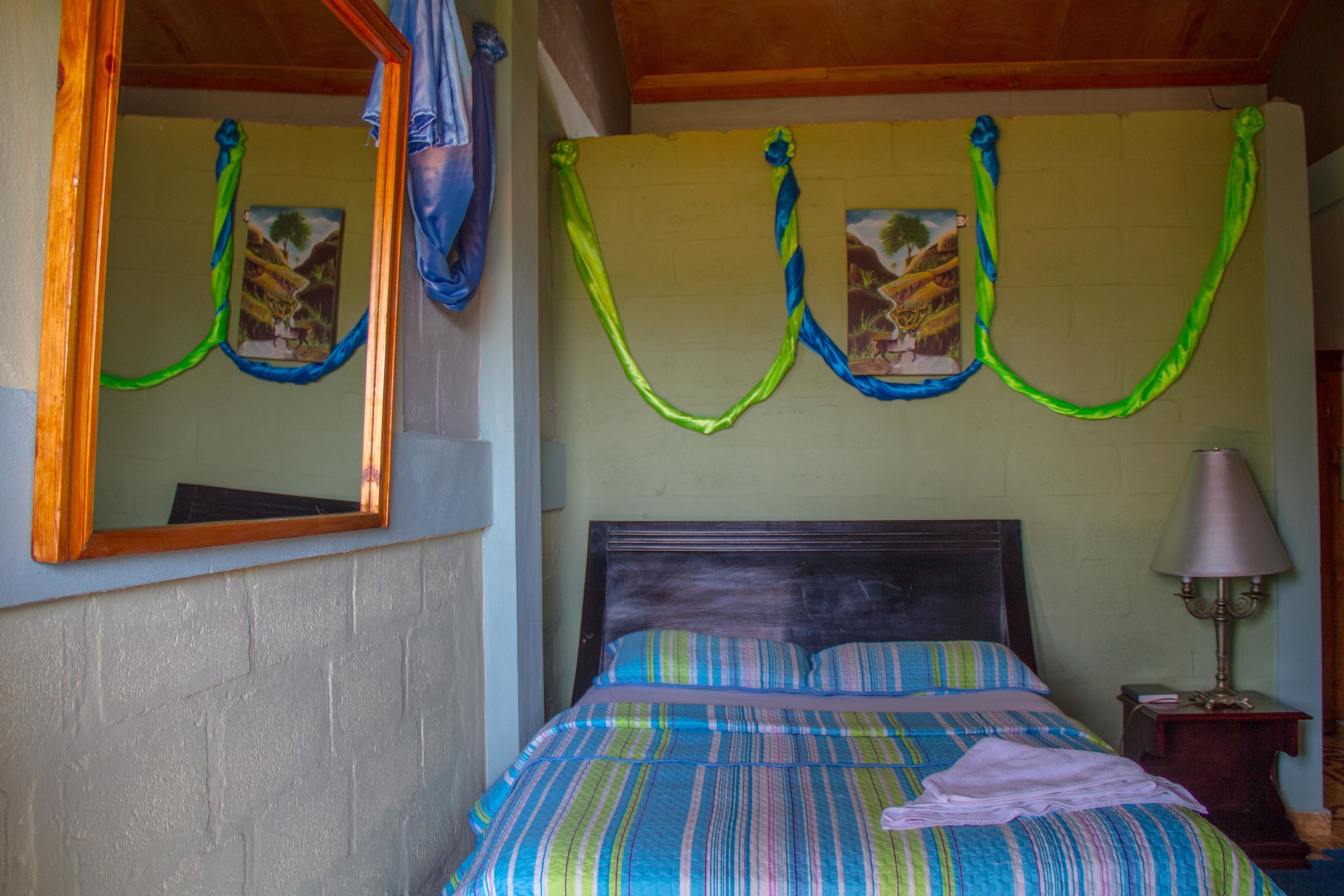 A bedroom with a bed, a nightstand, a lamp, and a mirror.