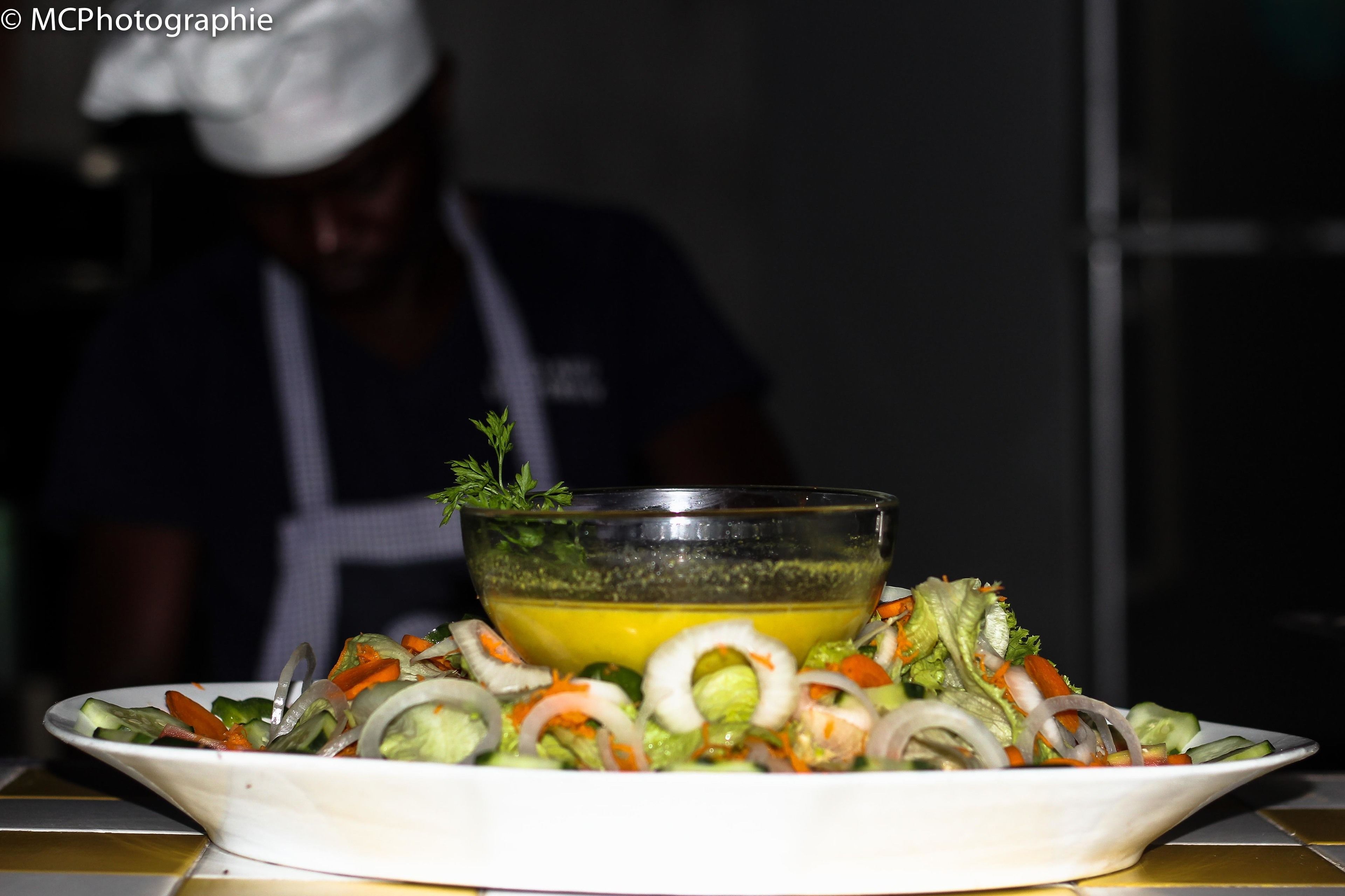 A plate of salad with a dressing bowl in the background.
