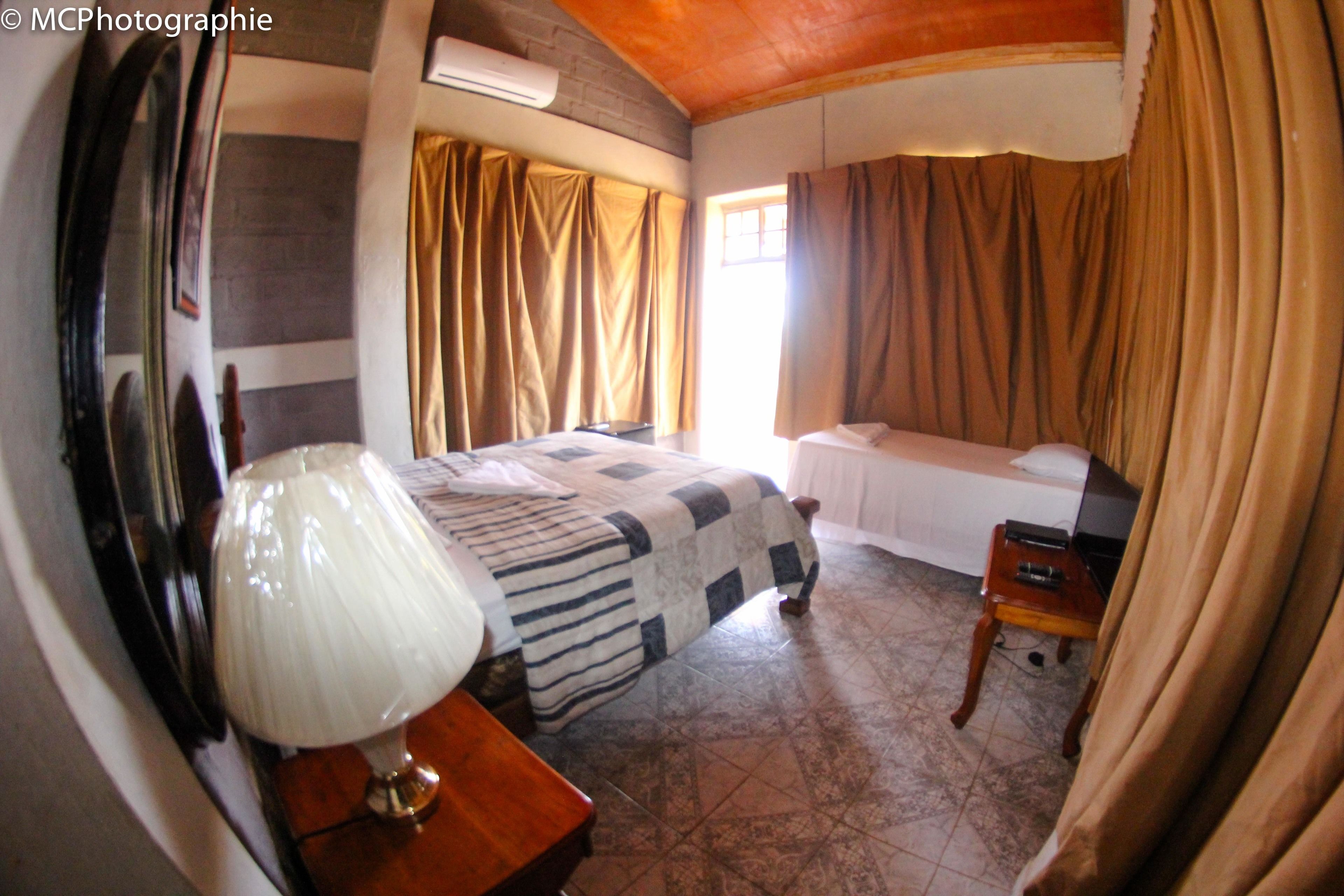 Un dormitorio con cama, mesita de noche, lámpara y ventana con cortinas.