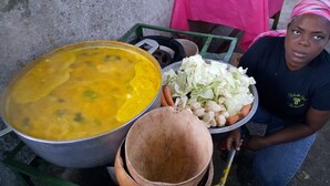 A person holding a large pot of soup, a bowl of vegetables, and a metal container.