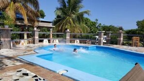 A swimming pool with a tiled deck, palm trees, and a clear blue sky. - Rollanda Hotel (Port-au-Prince)