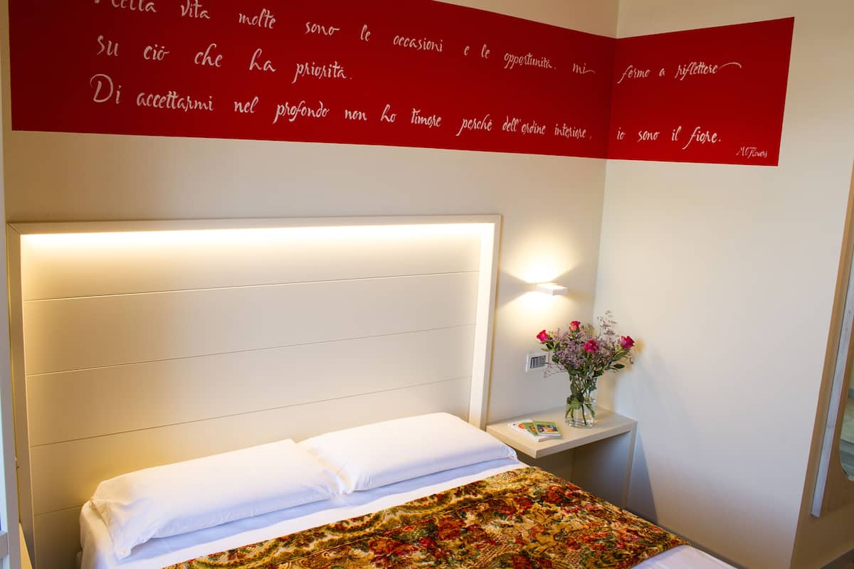 A neatly made bed with white linens, a floral-patterned blanket, and a bedside table with a vase of flowers.
