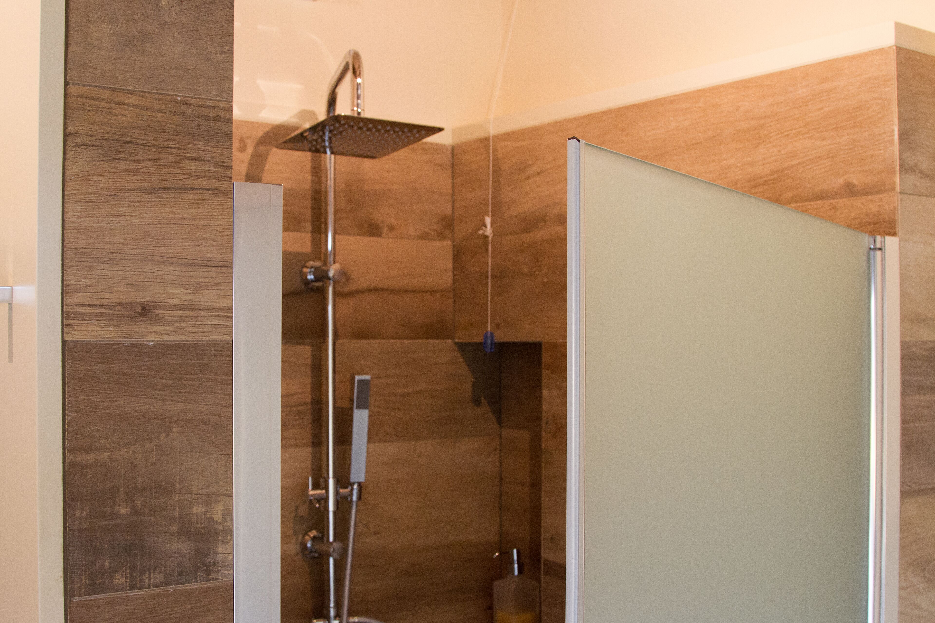 A modern shower with a square head, a handheld showerhead, and a wall-mounted control panel.