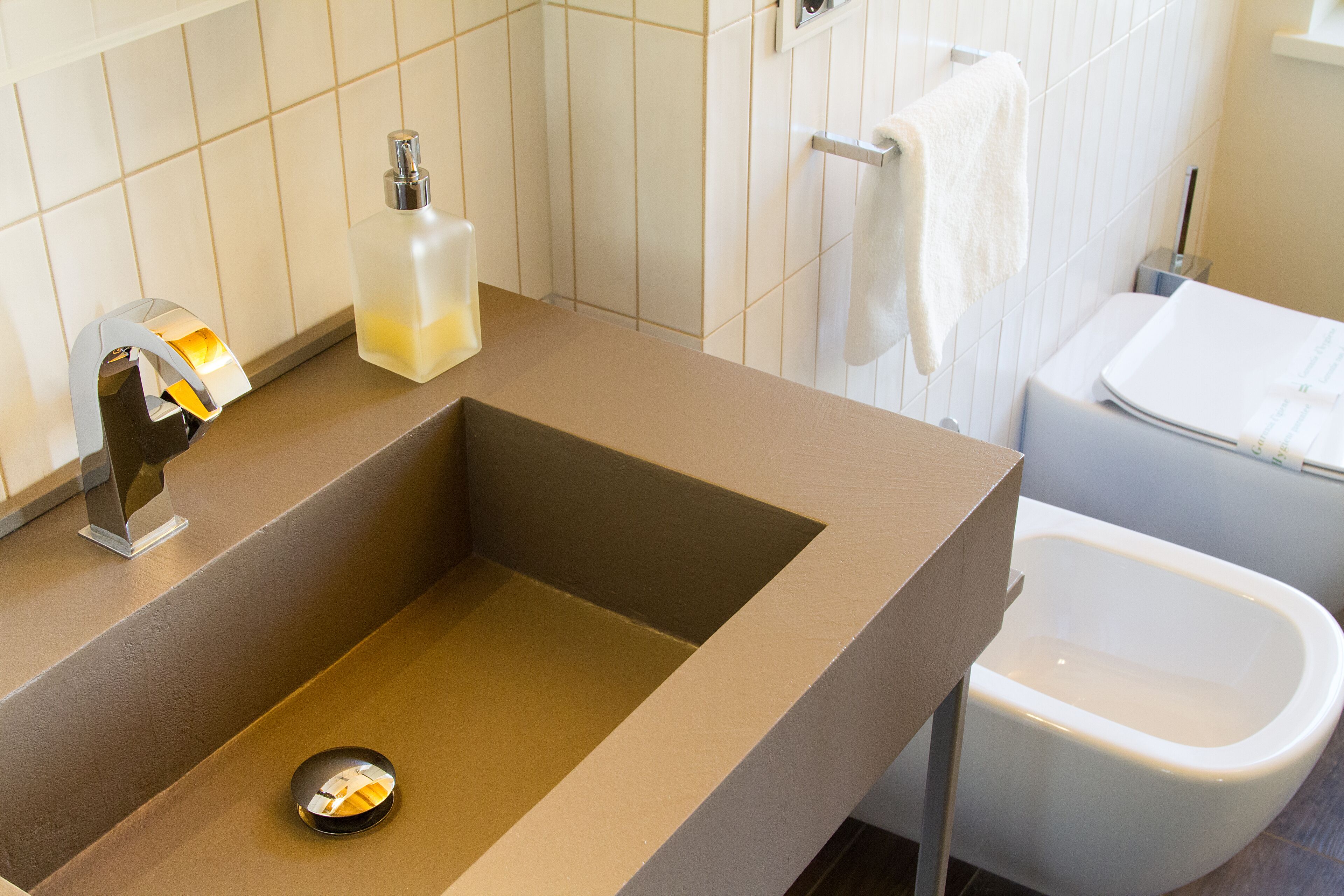 Une salle de bain avec un lavabo beige, un distributeur de savon, un porte-serviettes et des toilettes.