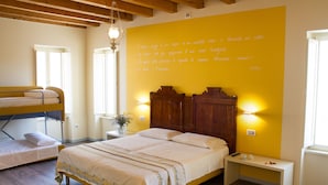 Une chambre avec un lit superposé, un lit simple, une table de chevet avec une lampe et un grand mur jaune orné de texte.