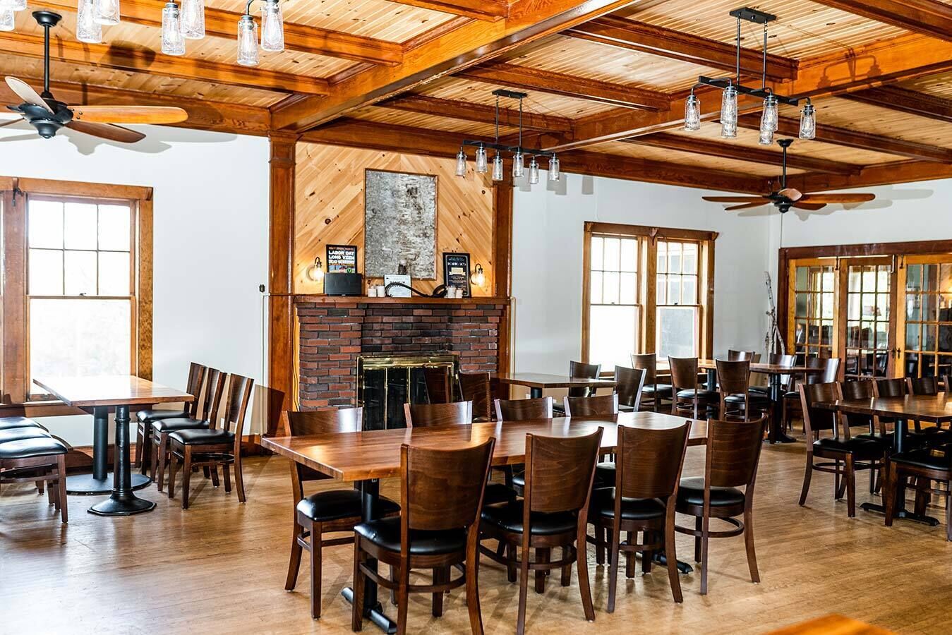 Un amplio comedor con mesas y sillas de madera, una chimenea de ladrillo y ventanas grandes.