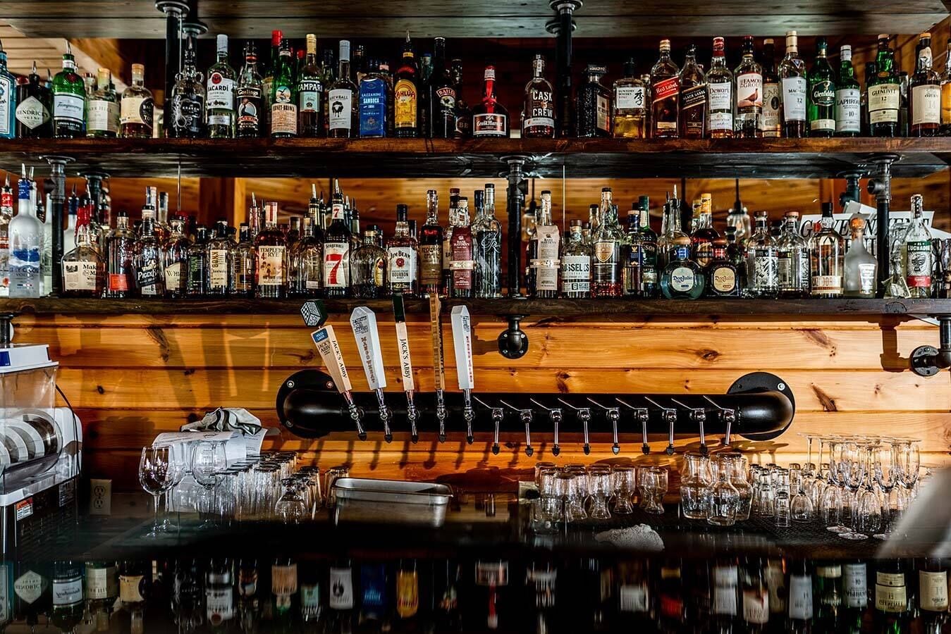 A bar with multiple shelves of liquor bottles and a variety of beer taps.