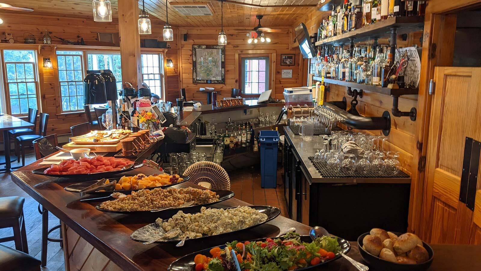 A buffet bar with various food items and a bar area with bottles and glasses.