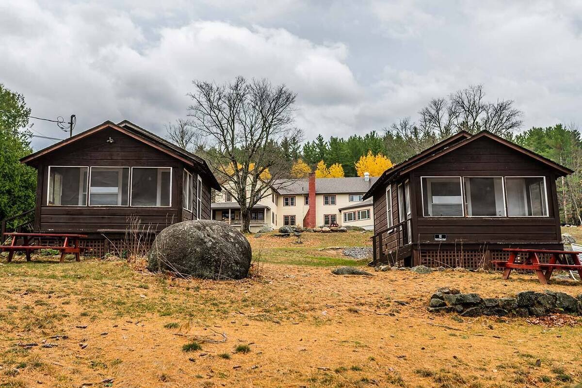 Deux cabanes en bois dotées de grandes fenêtres, une table de pique-nique et un gros rocher au premier plan.