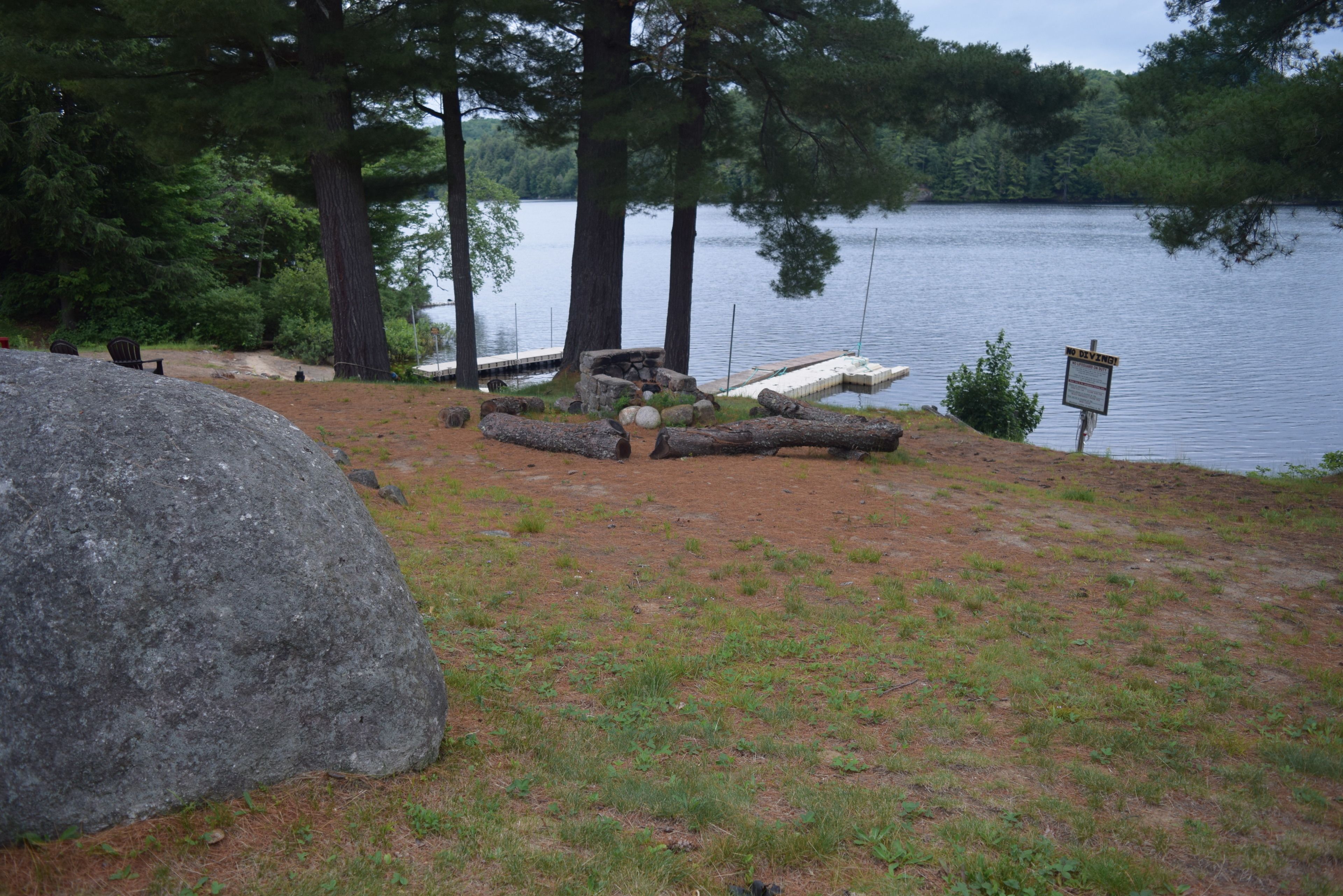 Un camping junto al lago con una gran roca, un pozo de fuego y un cartel que indica un área de picnic.
