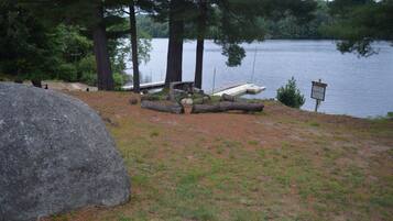 Un camping junto al lago con una gran roca, un pozo de fuego y un cartel que indica un área de picnic.