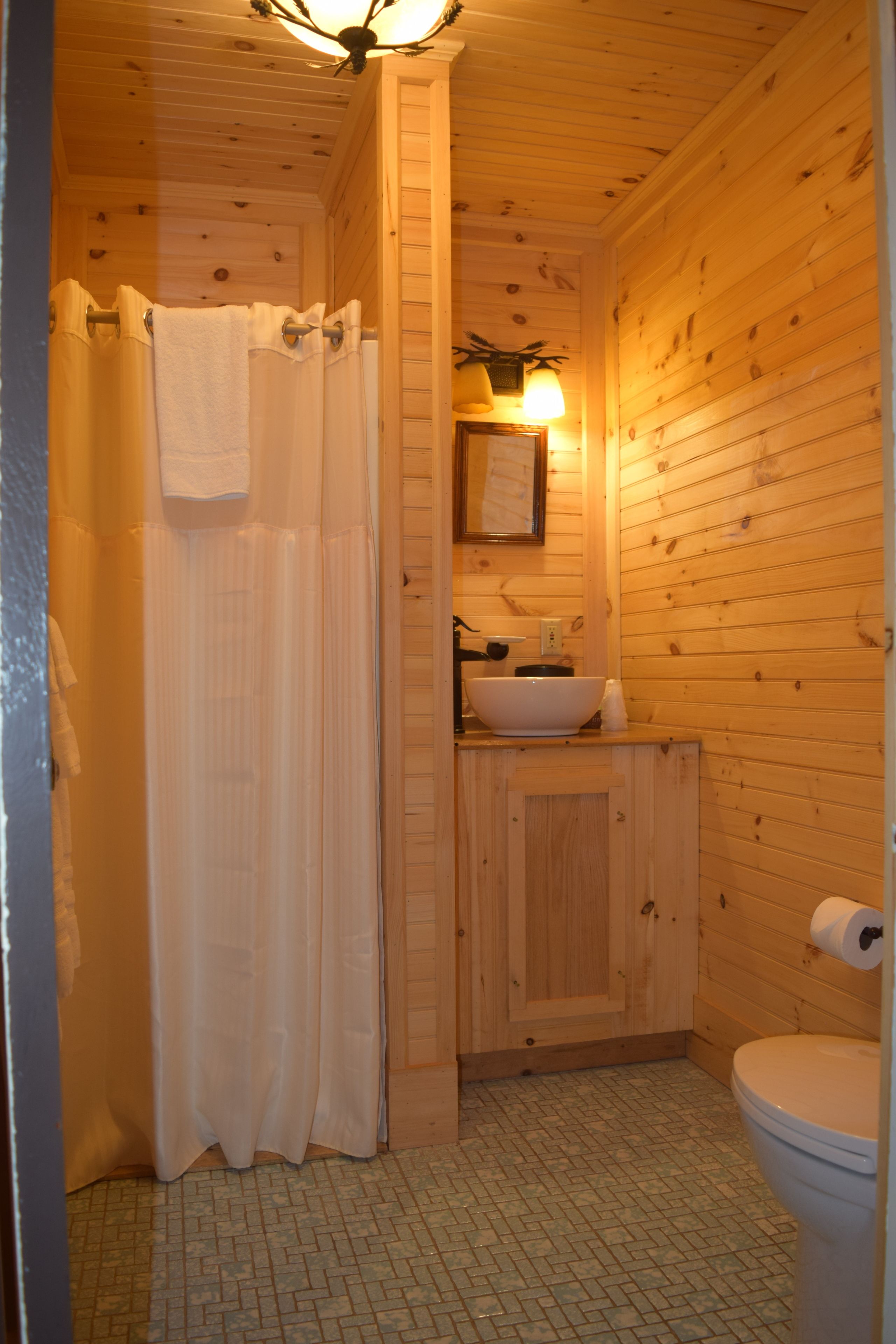 Un baño de cabaña de madera con cortina de ducha, lavamanos, inodoro e iluminación empotrada en la pared.