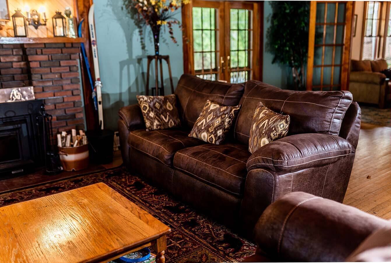 Un salón acogedor con un sofá de cuero, cojines estampados, una mesa de centro de madera y una chimenea.
