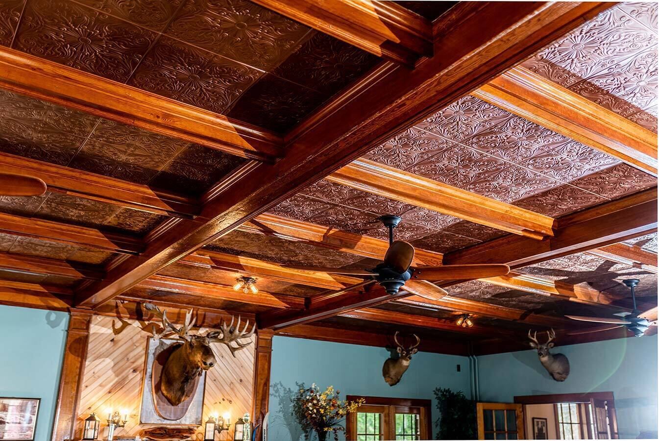 A room with wooden beams and a ceiling fan. There are mounted animal heads on the walls.