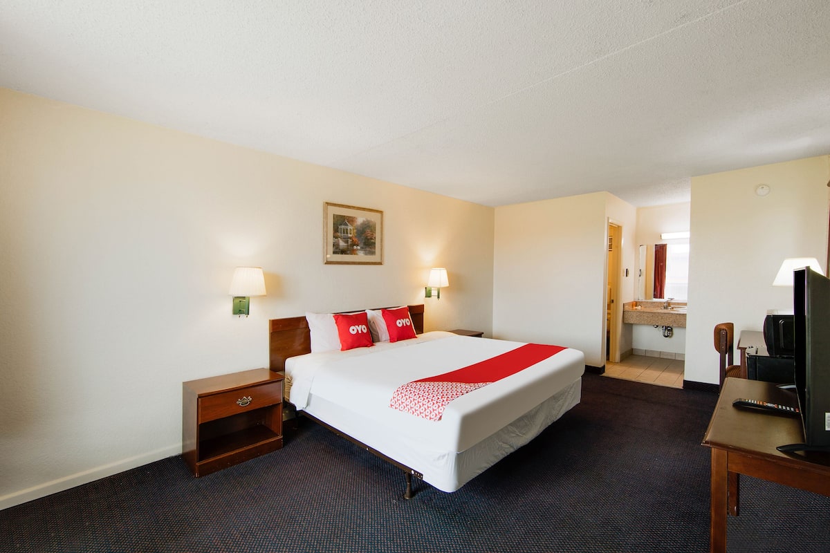 Une chambre d’hôtel avec un grand lit, des tables de chevet, un bureau avec une chaise, une télévision et une salle de bain visible à travers une porte ouverte.